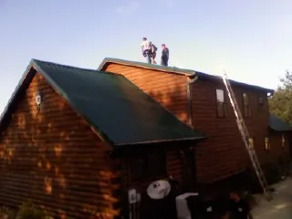 Crew on the ridge of a green metal roof on a two story log home in Decatur